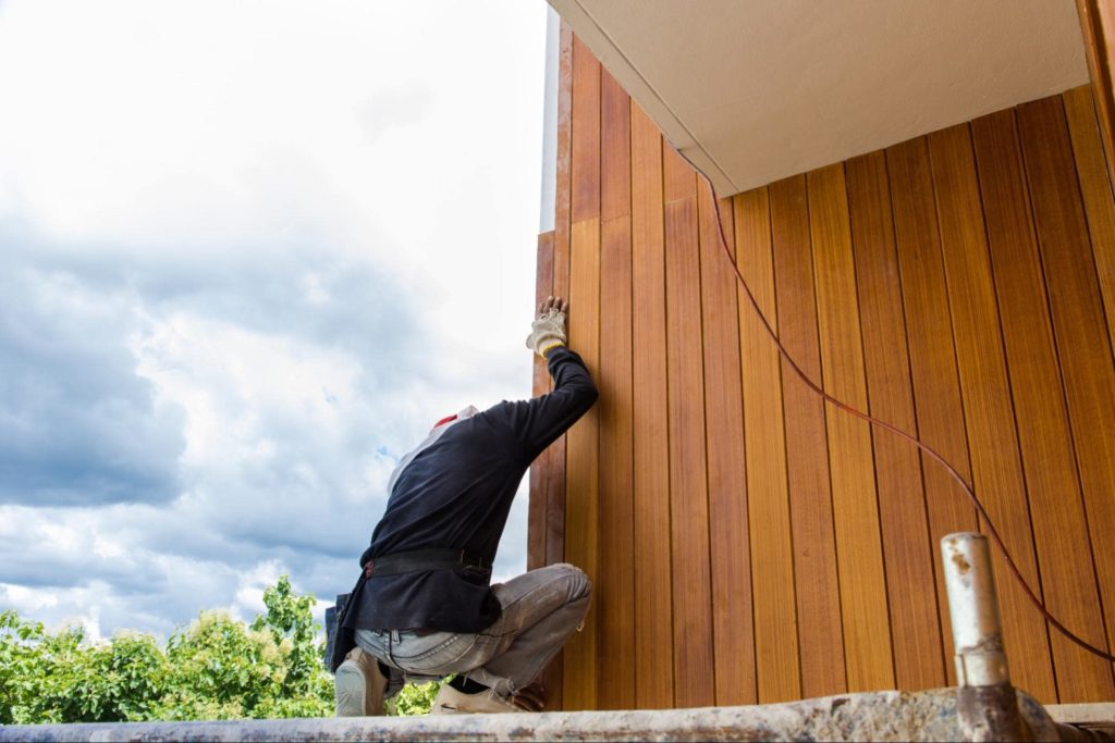 A picture of a man sanding modified wood siding on a home.