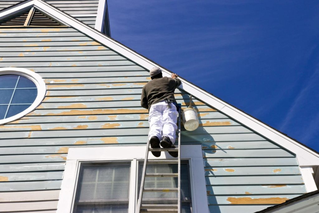 A picture of a man on a ladder working on a distressed house.