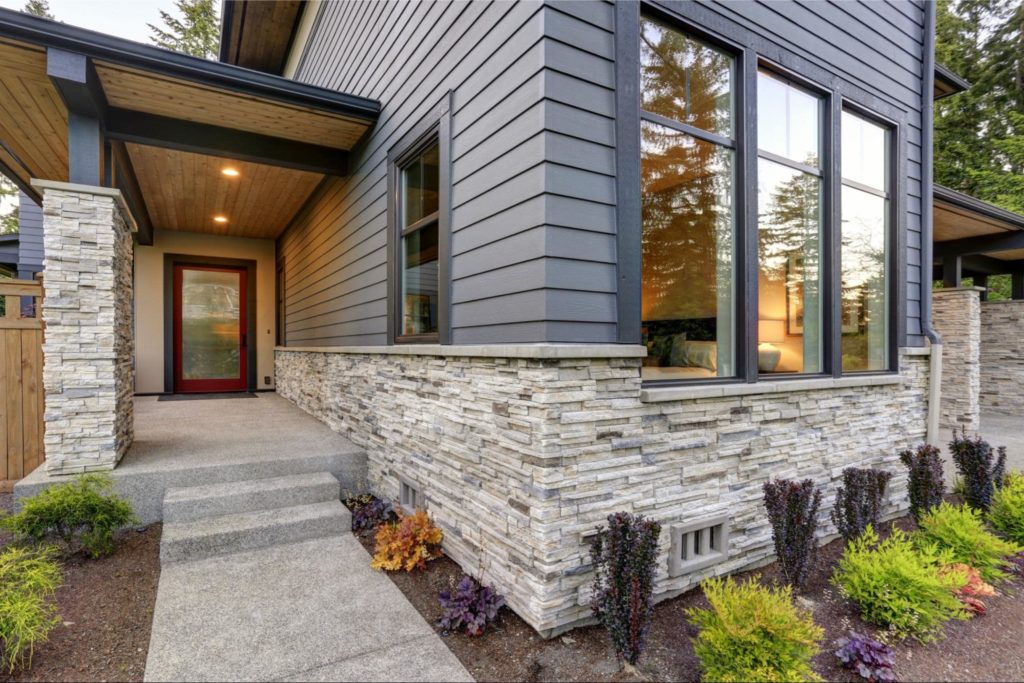 A picture of a home with stone veneer siding and a small garden in front of the home.