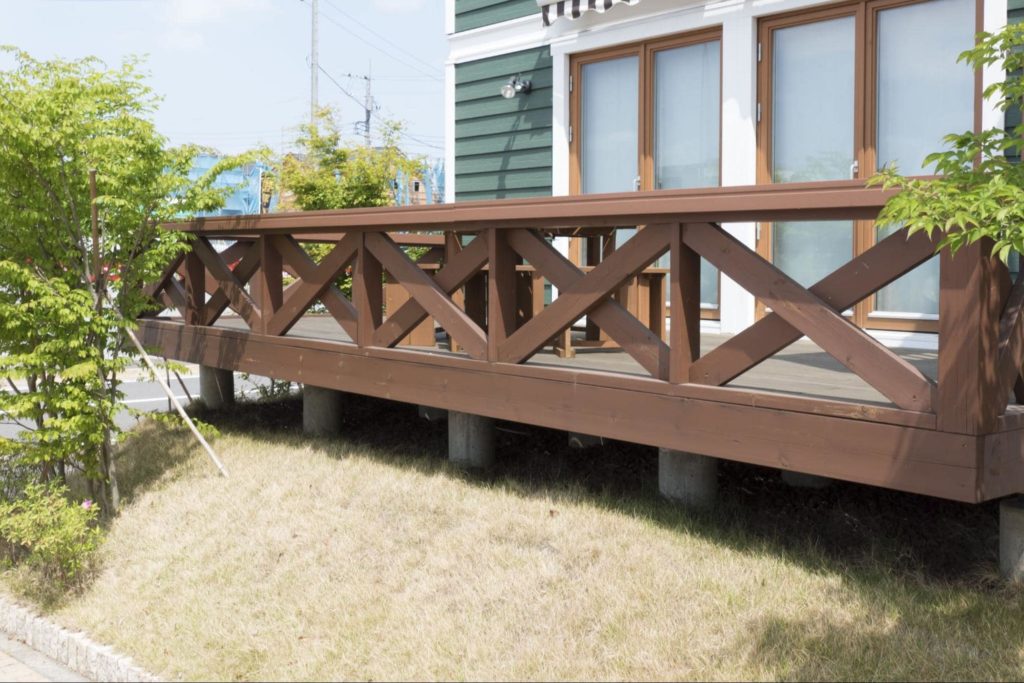 A picture of a raised brown deck attached to a house with vinyl siding.