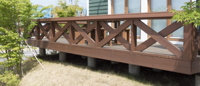 A two-story brown deck attached to a house with vinyl siding.