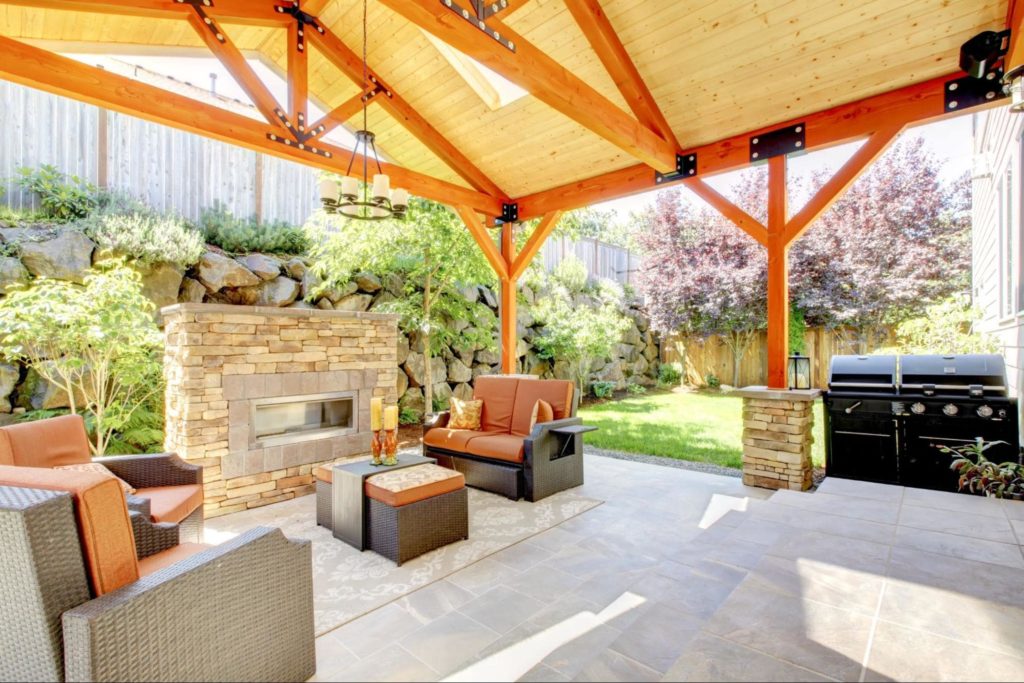 A picture of a covered deck with a stone fireplace and outdoor patio furniture.