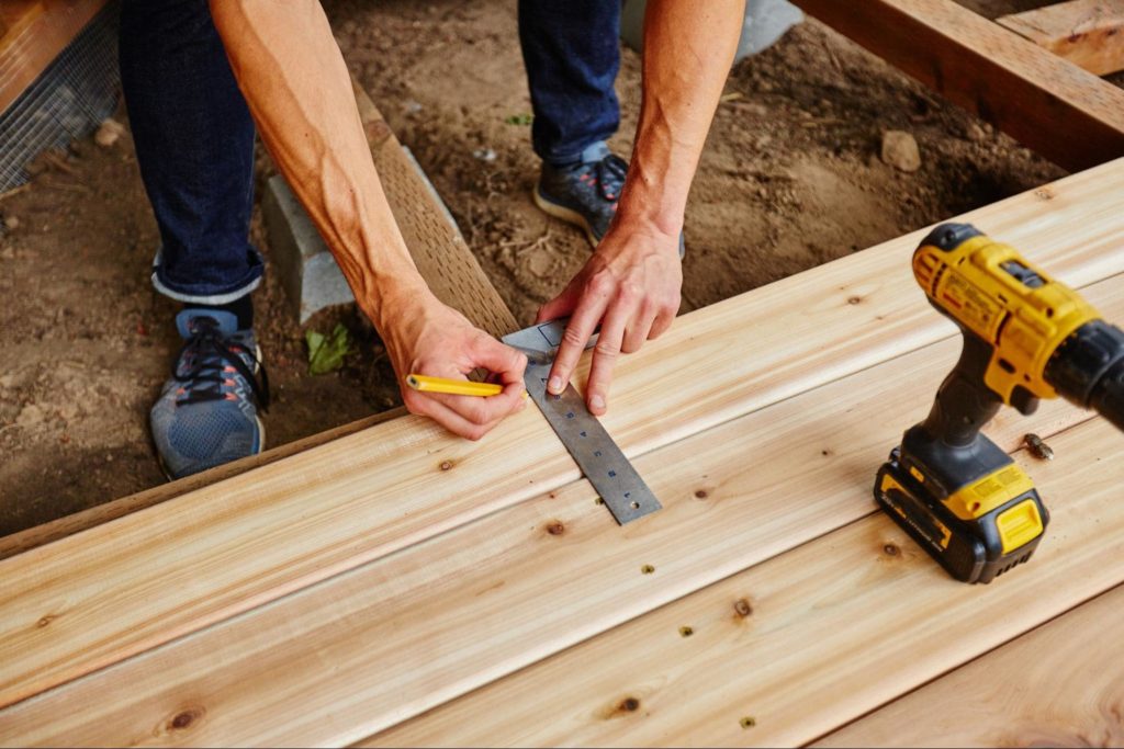 A picture of a construction using a ruler and marking his measurements on a piece of wood.