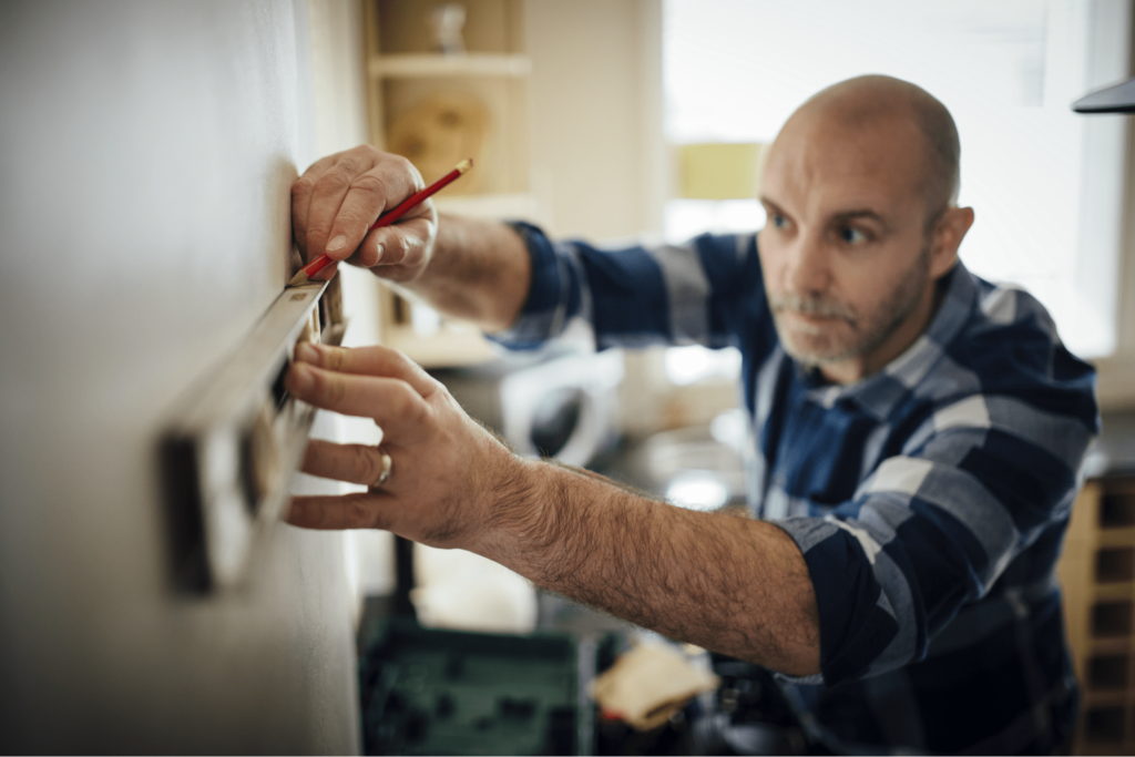 A picture of a man in a flannel shirt using a level to mark out a specific dimension on a wall.