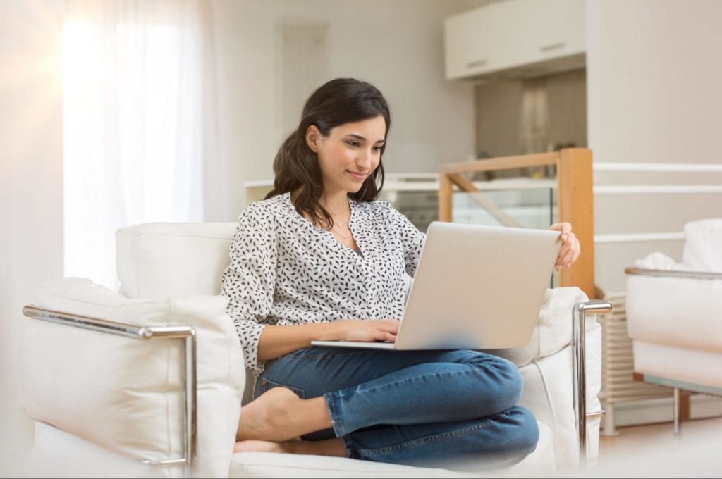 A woman peacefully sitting on the couch with a laptop.