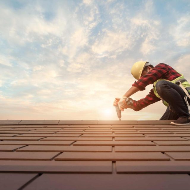 A contractor in a hard hat repairing a roof with a nail gun.