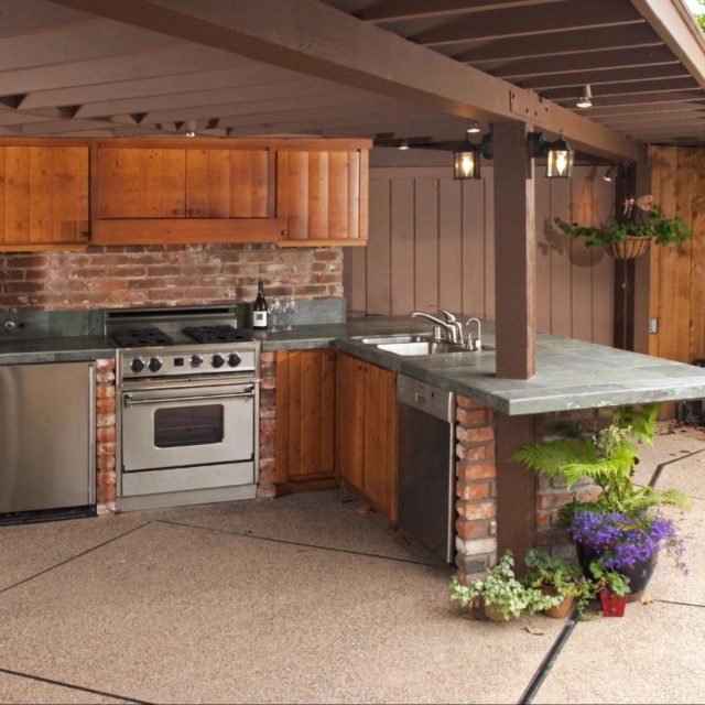 An outdoor kitchen with wood cabinets and potted plants as decorative additions.