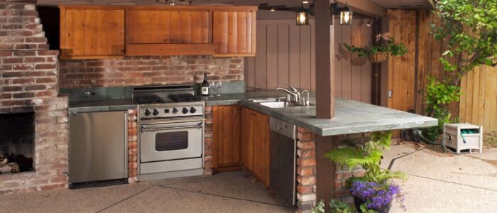 An outdoor kitchen with wood cabinets and potted plants as decorative additions.