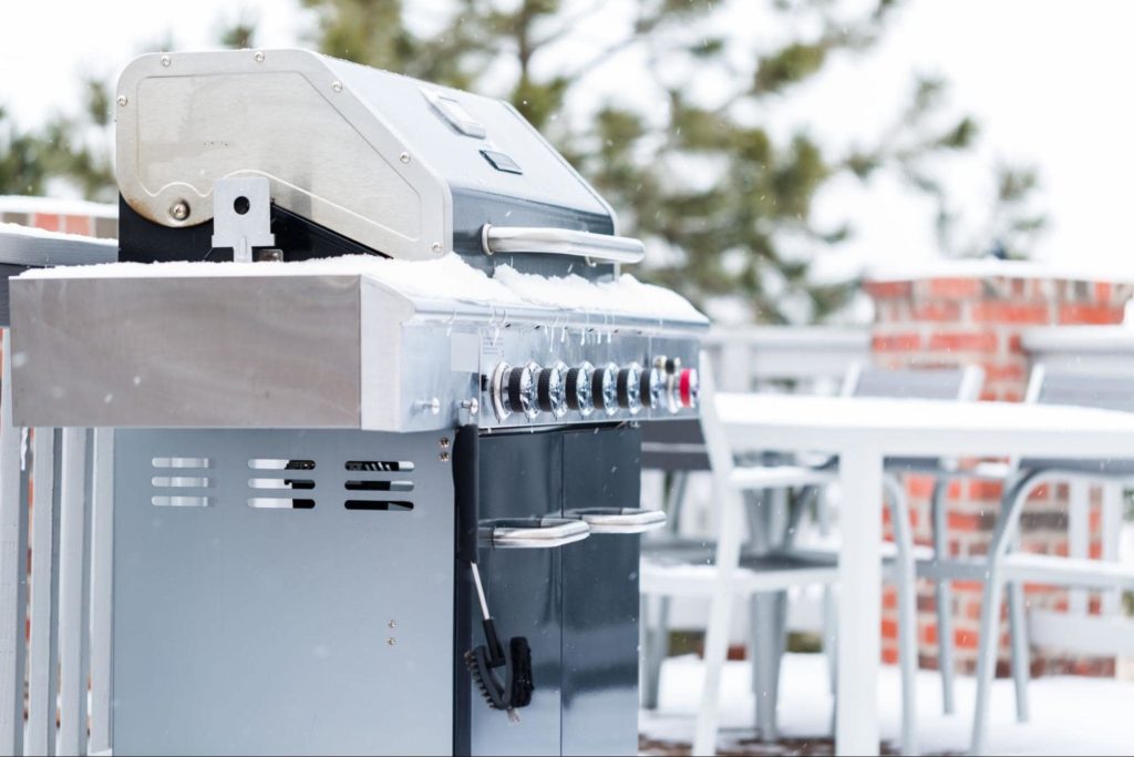 A picture of a grill sitting outside in the snow.
