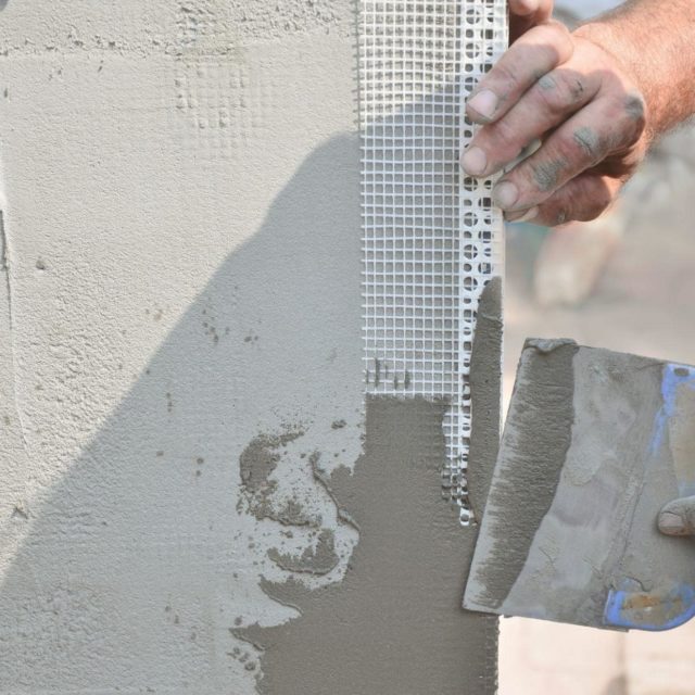 A picture of a hand applying stucco to the outside of a home.