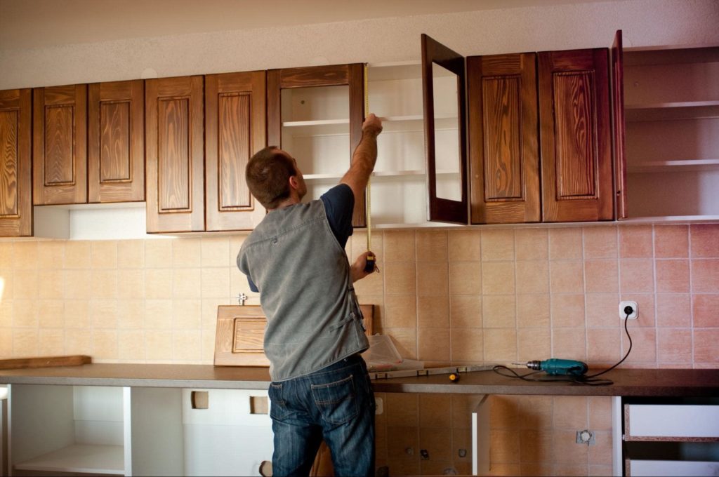 A contractor installing wood cabinets in a kitchen.