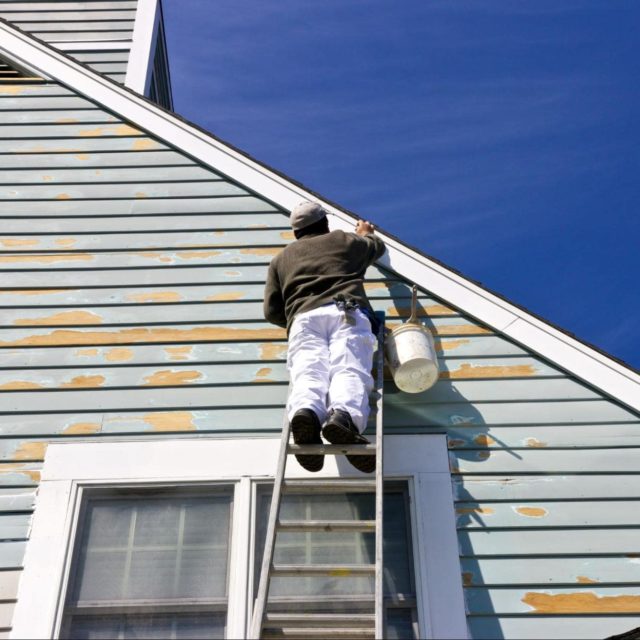 A contractor on a ladder working on updating a home's siding.