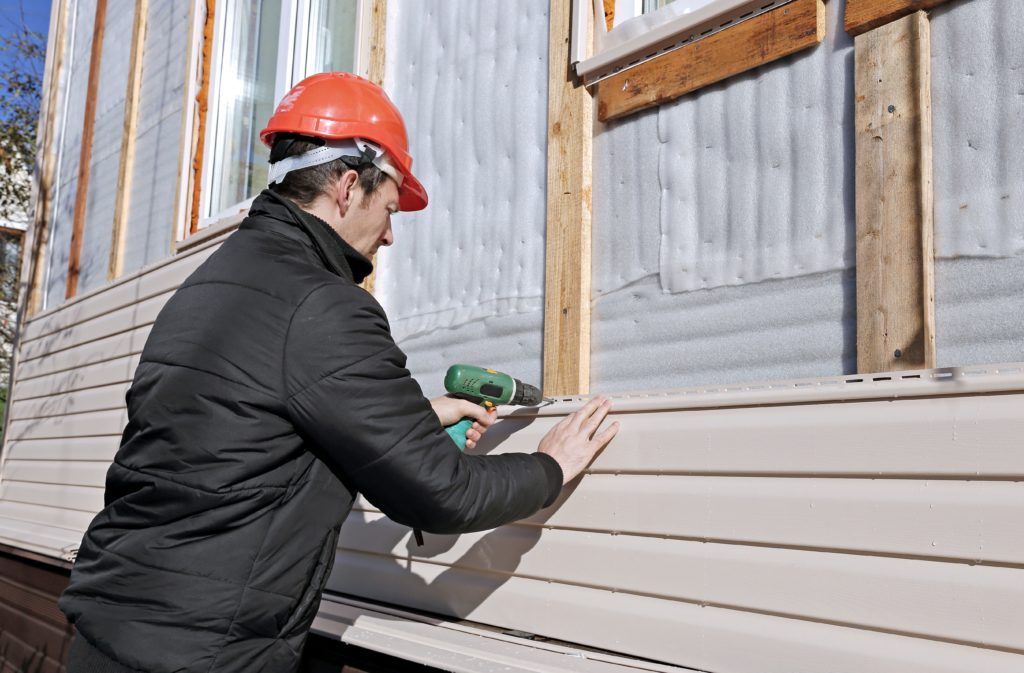 A man installing vinyl siding on a house.