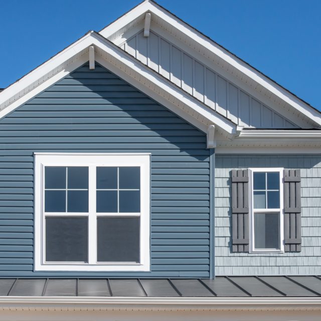 The top windows on a house with blue vinyl siding.