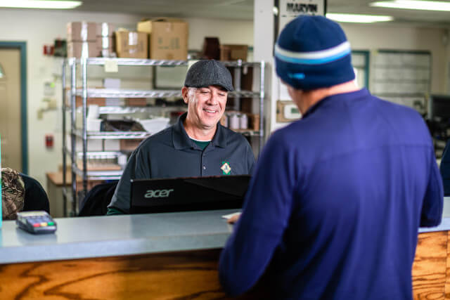 worker smiling behind the counter looking at computer and helping customer