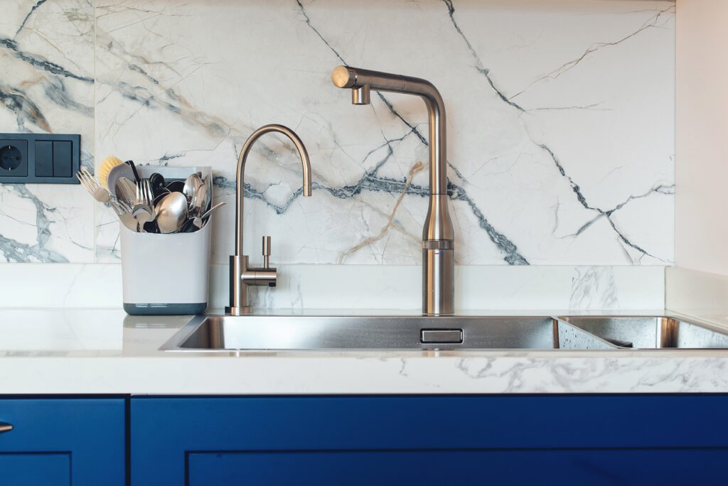 A stainless steel faucet with a granite backdrop and blue cabinets.