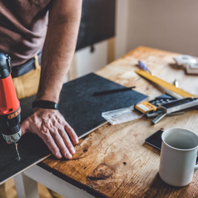 A man drilling a hole through a piece of wood during a best ROI home renovation.