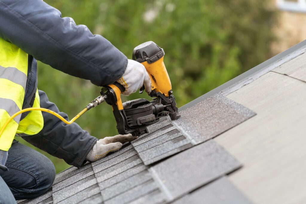 Someone using a roofing nail gun to attach shingles to a roof.