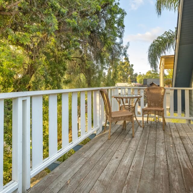 An image of a wooden deck with a table and two chairs in the corner.