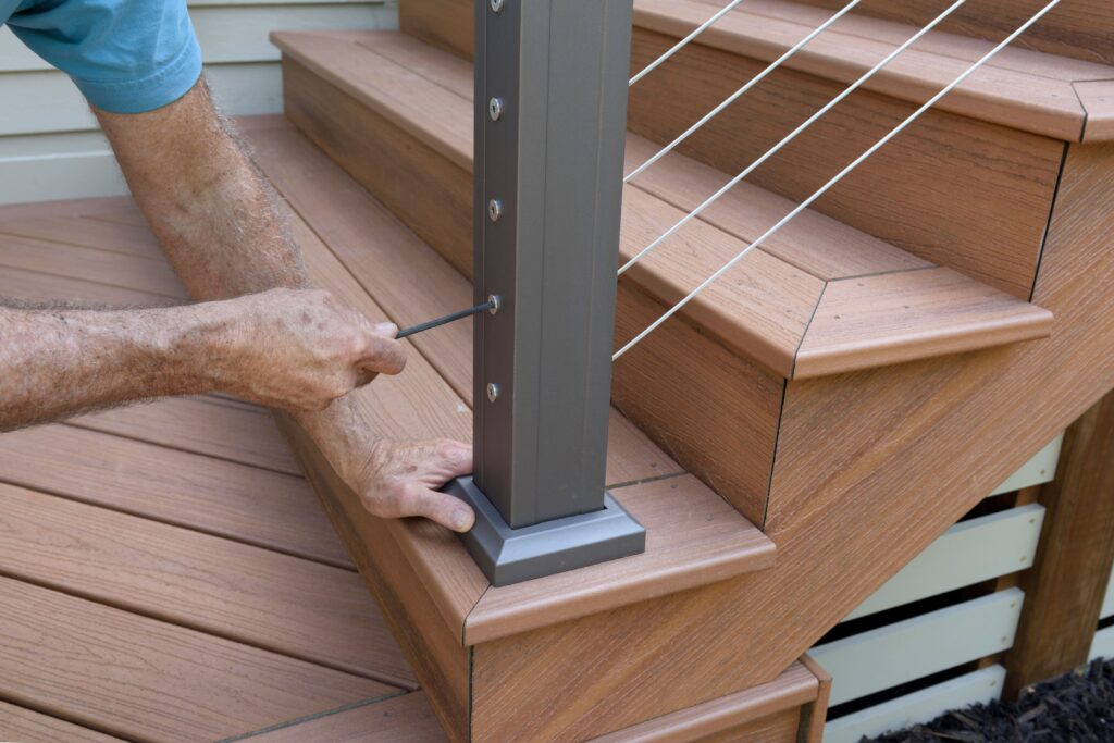 A man working to install a cable railing on a set of deck stairs.