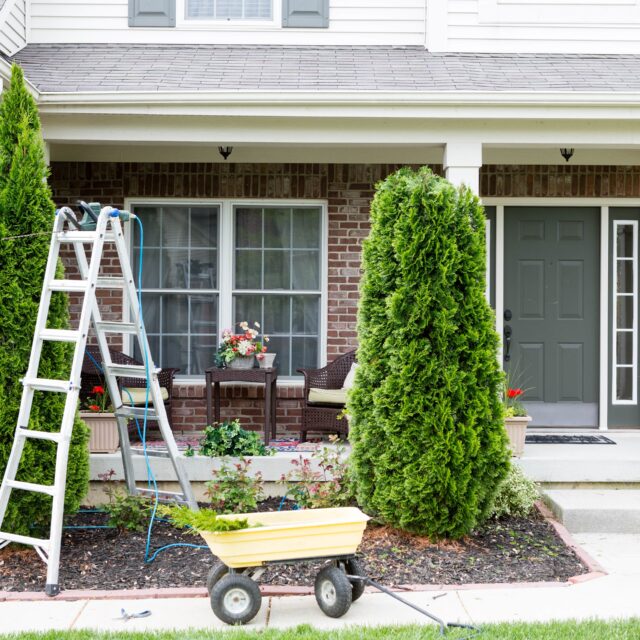 The front of a home where someone is doing maintenance with a ladder and garden cart