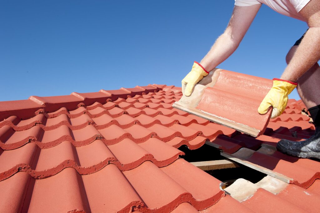 A man replacing terracotta roof tiles.