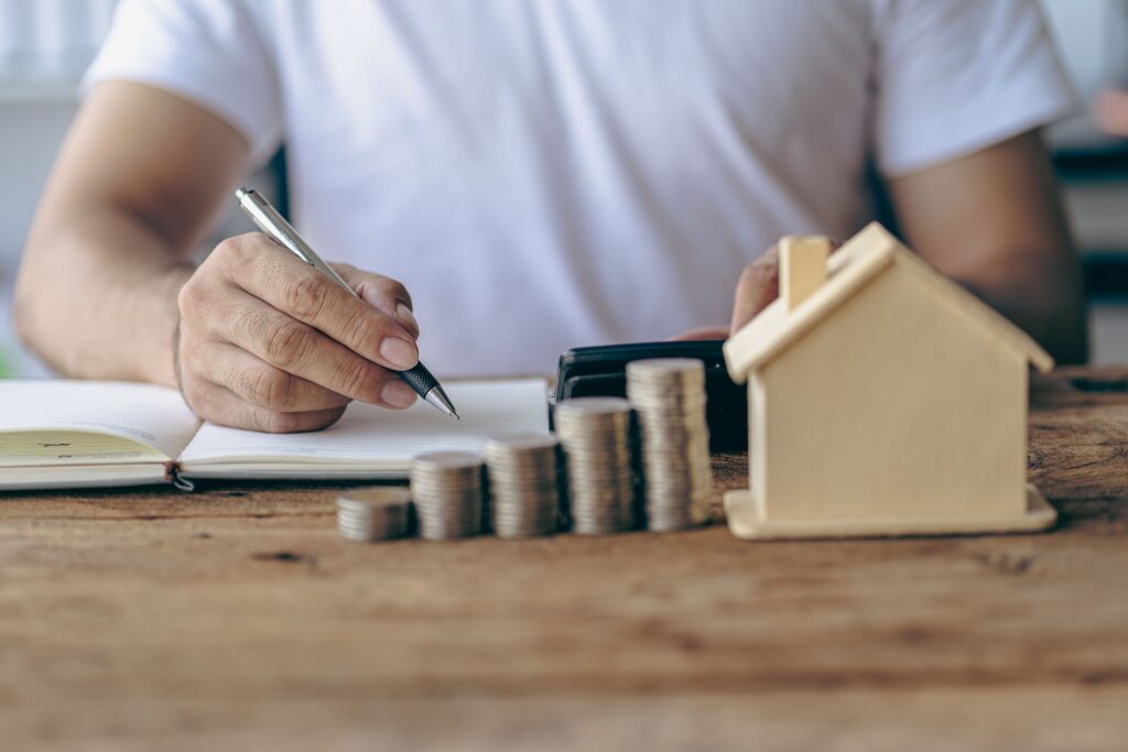 A person sitting trying to create a budget with a house model and money sitting in front of them.