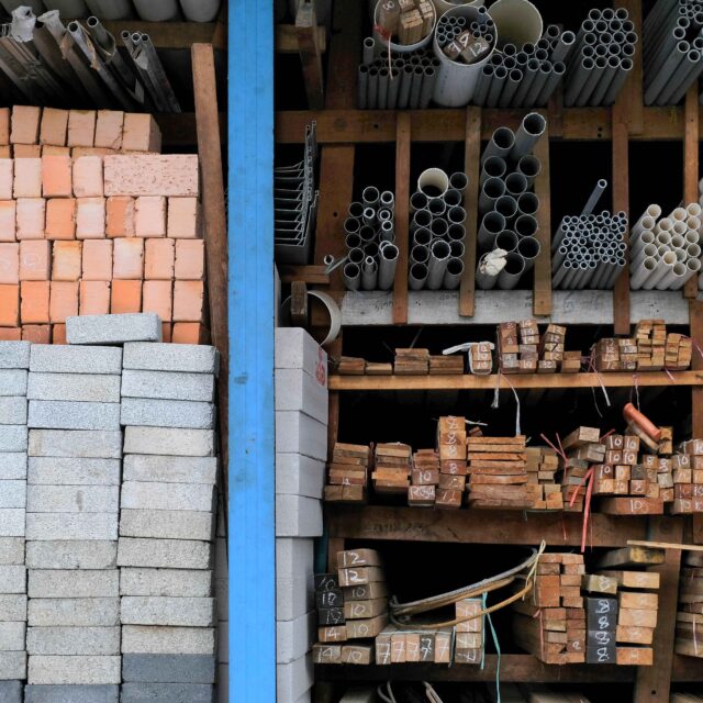 An image of building materials in storage, including bricks, paving stones, pipes, and pieces of wood.