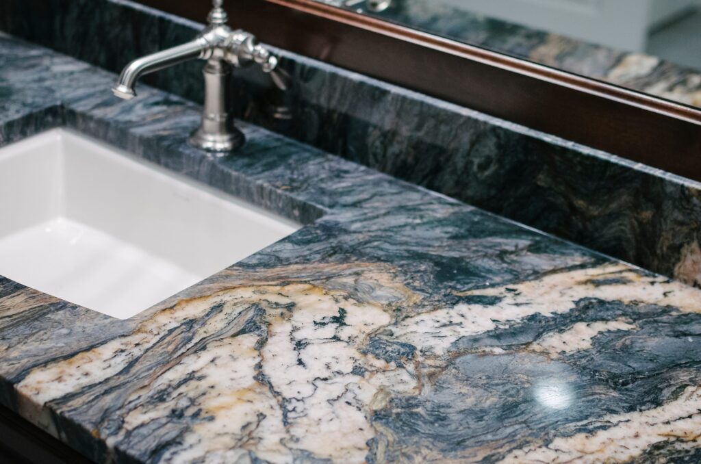 An image of a granite countertop with a silver faucet and white porcelain sink.