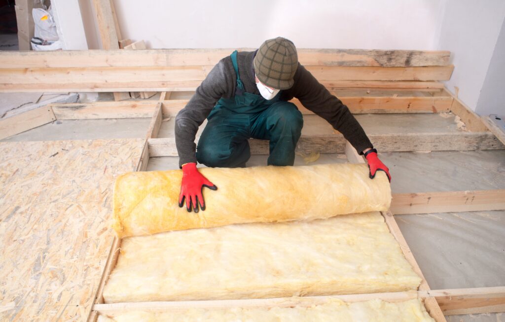 A construction worker rolling out insulation for a room. 