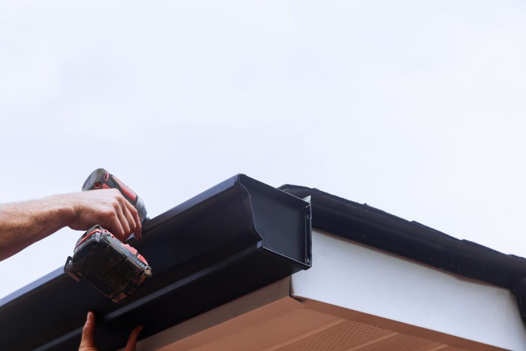 A person holding a drill  installing gutters on a roof